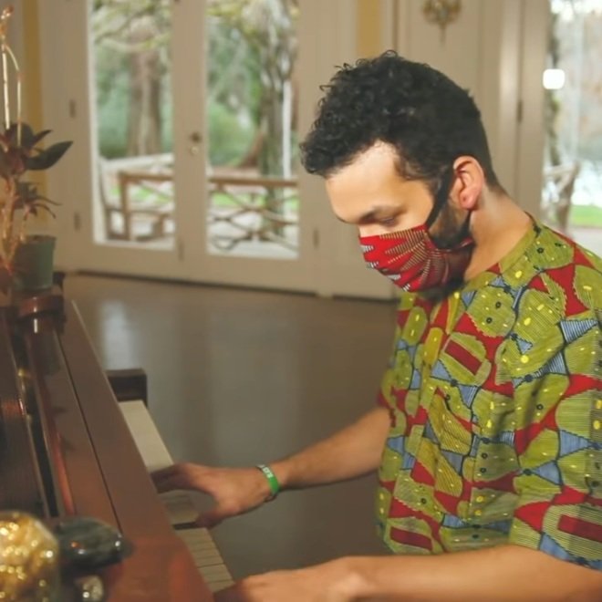 A man playing the piano and wearing a red mask