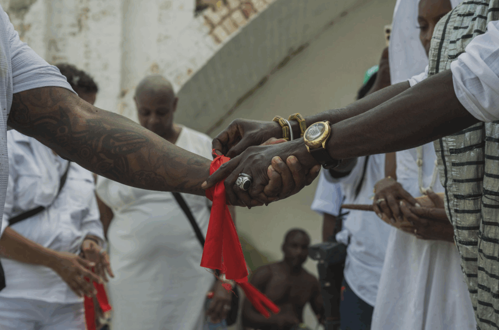 Arms of three black people, holding each others hands, and holding a red cloth.
