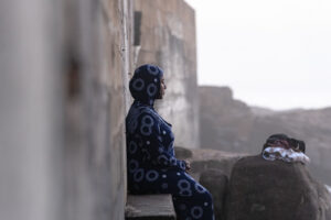 A woman sitting by a stone wall, staring out into the ocean during the 2026 South Africa Homeward Journey.