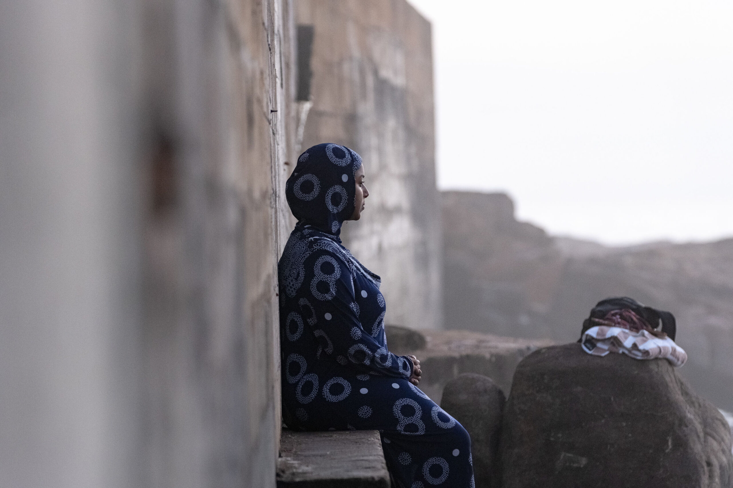 A woman sitting by a stone wall, staring out into the ocean during the 2026 South Africa Homeward Journey.